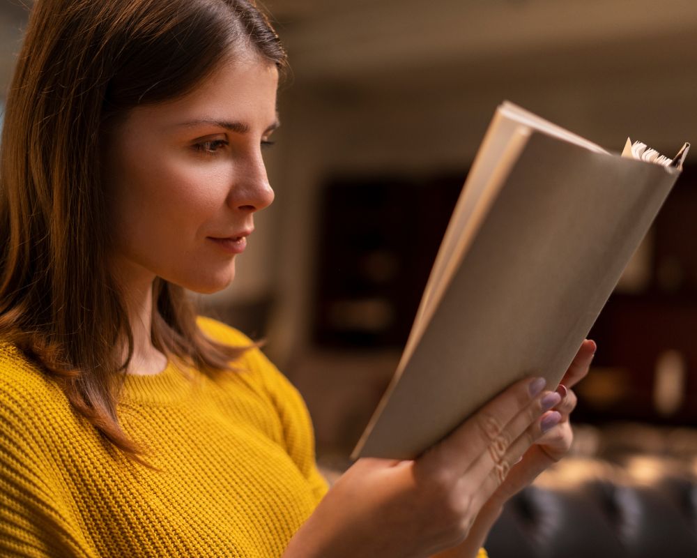 Mujer mirando las páginas de un libro abierto, sosteniéndolo con ambas manos luego de aprender cómo convertir un manuscrito en un libro.